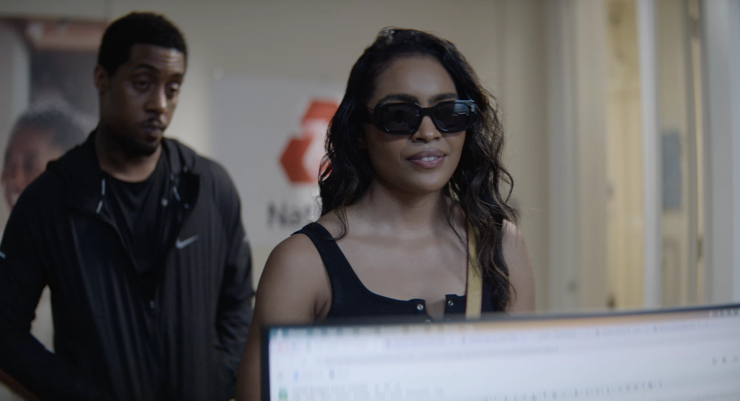 A woman wearing sunglasses stands at a counter with a man behind her.